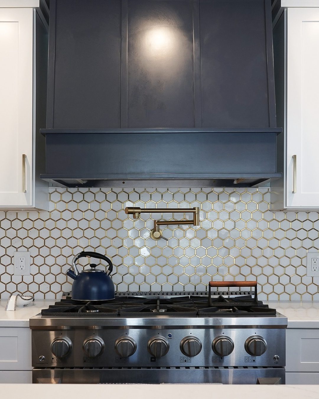 Berlin Kitchen with new hood Close-up of modern kitchen remodel featuring stainless steel gas range, navy blue custom range hood, gold pot filler faucet, and white hexagonal tile backsplash with gold accents — Central Connecticut Building and Remodeling, Berlin, CT.