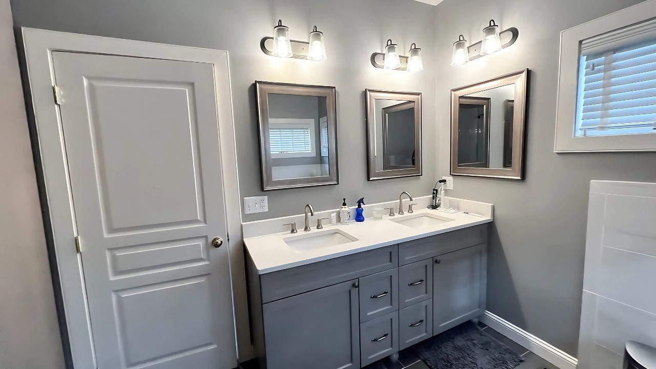 Double vanity installation with brushed nickel fixtures and framed mirrors in a remodeled Berlin, CT bathroom featuring soft gray walls and modern lighting.